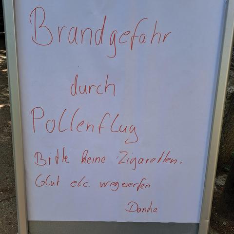 Schild mit der Aufschrift "Brandgefahr durch Pollenflug.  Bitte keine Zigaretten, Glut etc. Wegwerfen"