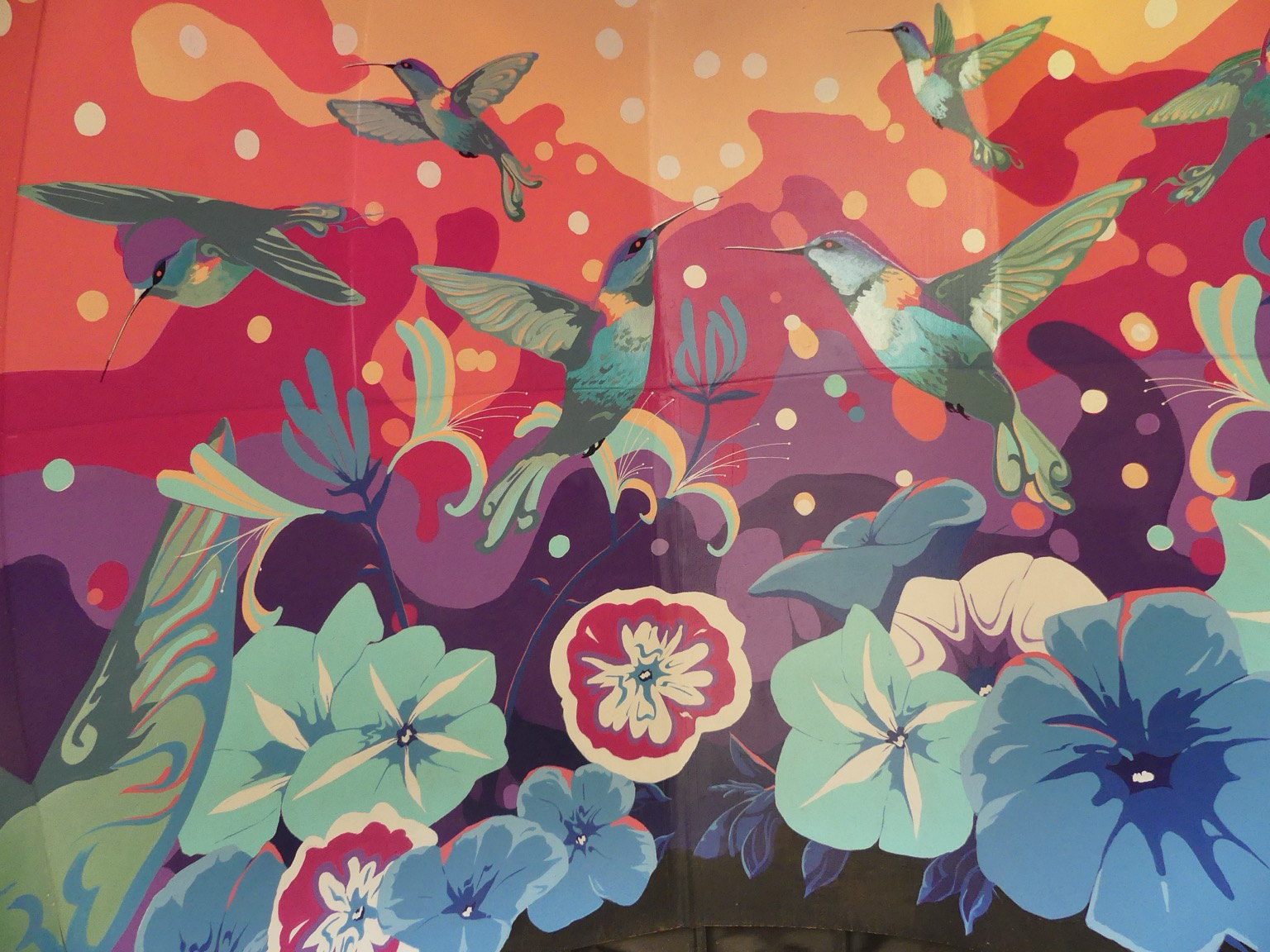 The inside of a little thatched hut, the walls painted with colorful flowers and hummingbirds in a sort of psychedelic style
