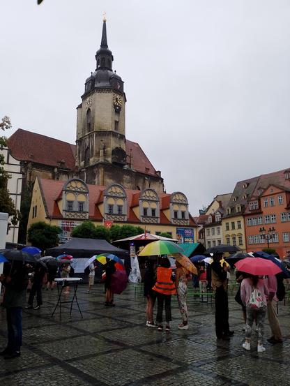 Menschen mit Schirmen, teils Regenbogen-geschmückt, auf dem Naumburger Markt