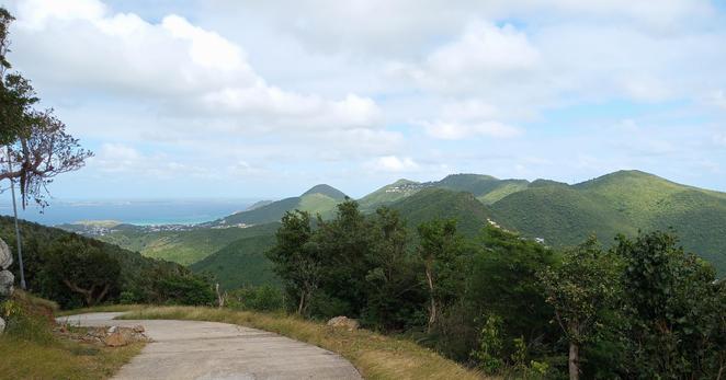 Von einem Betonweg aus Aussicht auf grüne Berge, links das Meer und in der Ferne die Insel Anguilla